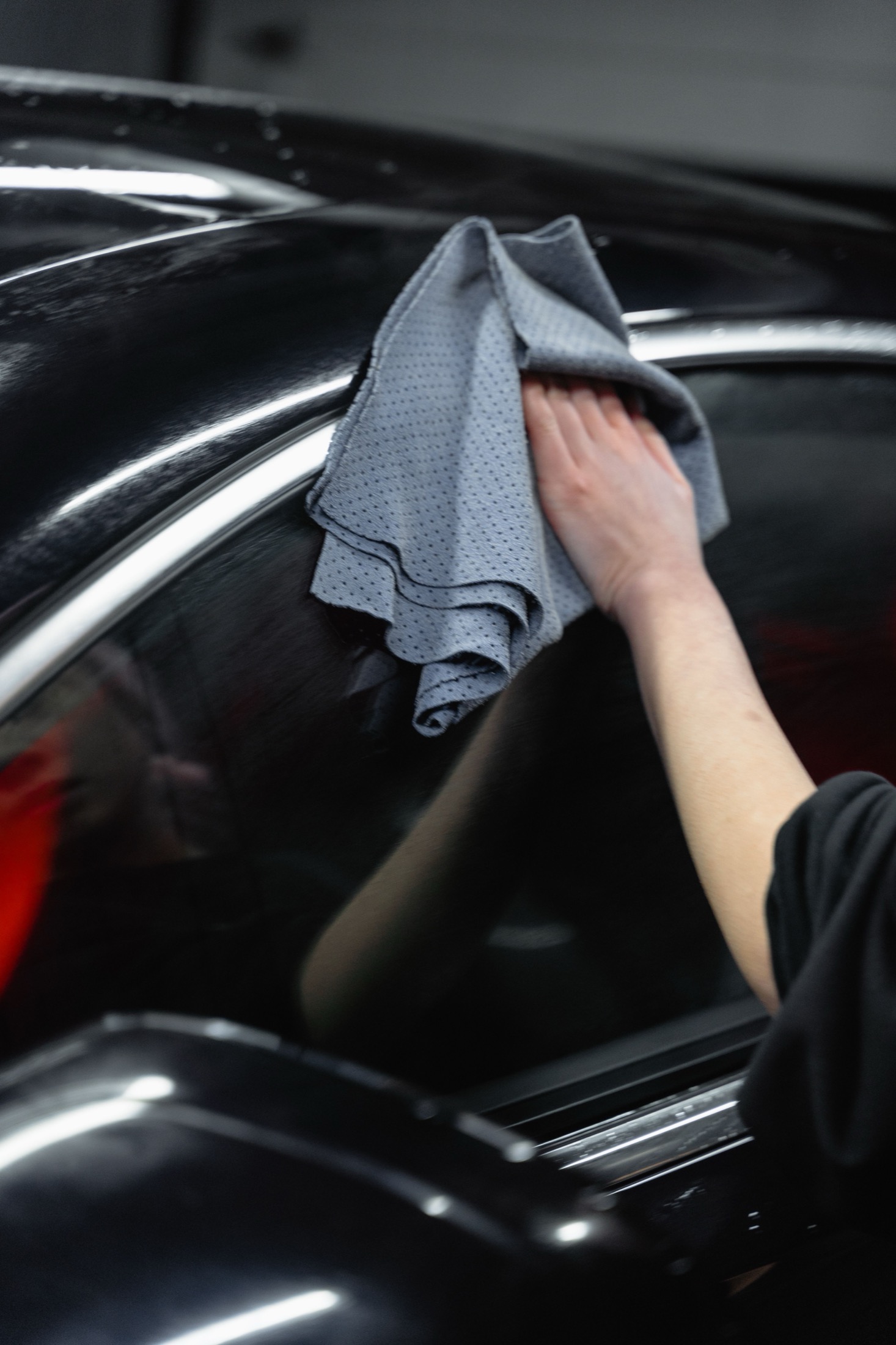 A black car panel being wiped with a microfiber cloth